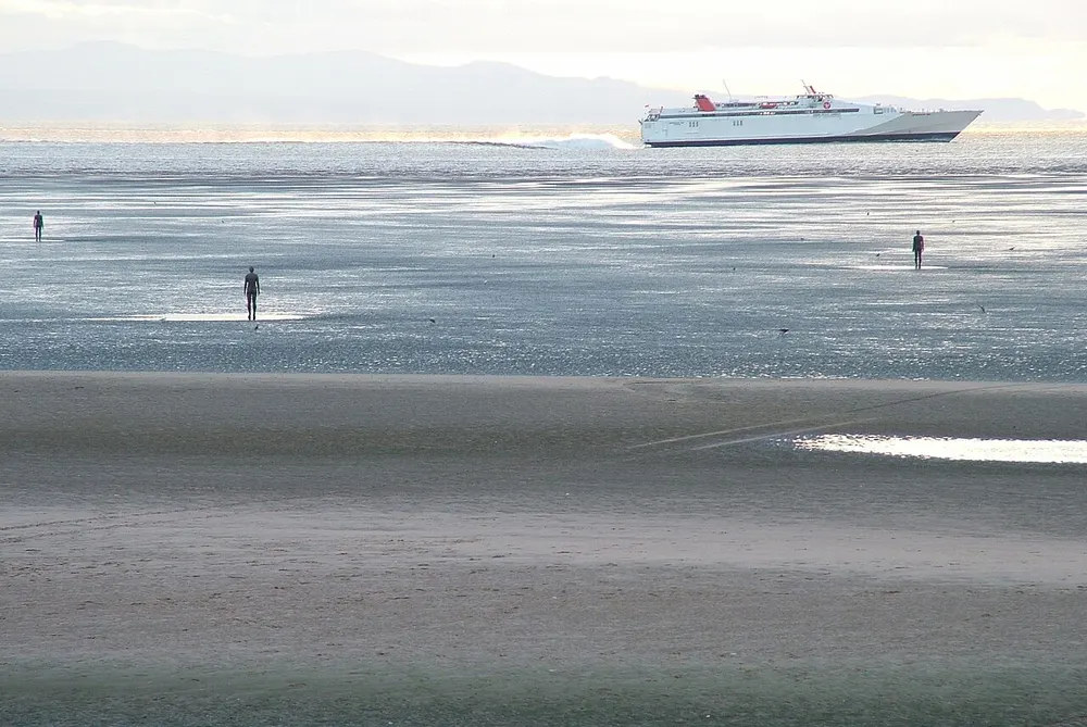 One of Antony Gormley's iron figures standing on the sand at Crosby Beach